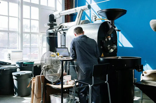 Torréfacteur en atelier devant une machine de torréfaction industrielle, en train de contrôler la qualité du café sur ordinateur.