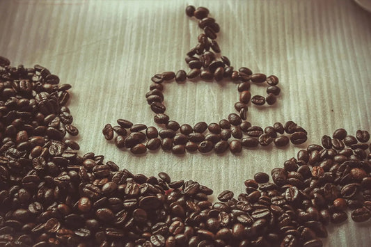 Illustration en grains de café formant la silhouette d'une tasse avec de la vapeur, posée sur une surface texturée en bois clair